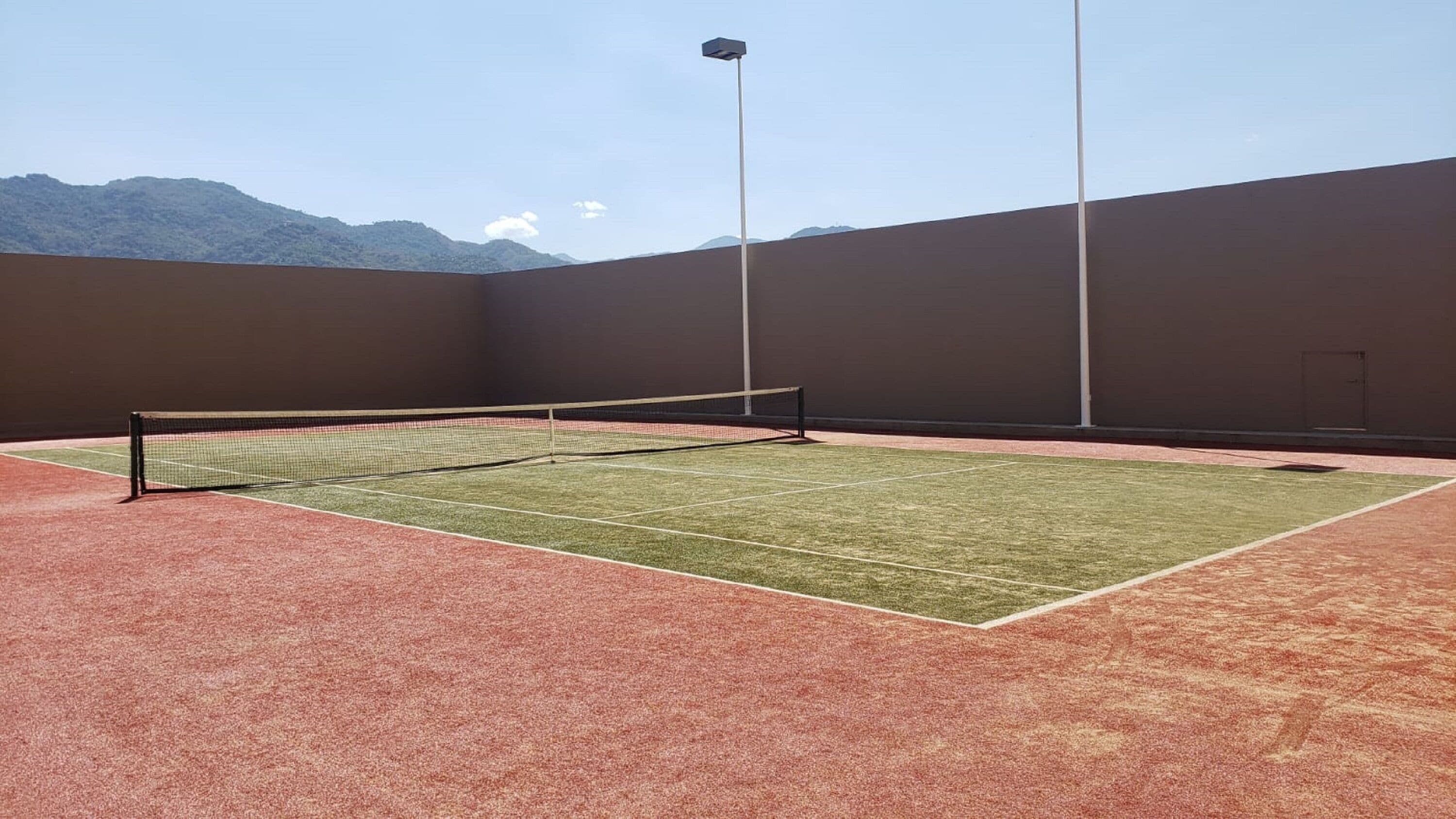 Un court de tennis intérieur, doté d’un filet, entouré de murs et offrant une vue sur la montagne.