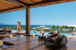 A couple on a wooden deck overlooking a pool with lounge chairs and a view of the ocean and resort buildings. - Secrets Vallarta Bay Puerto Vallarta - All Inclusive (Puerto Vallarta)