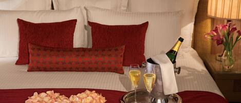 A neatly made bed with red and white bedding, a tray with champagne glasses, and a bouquet of flowers.