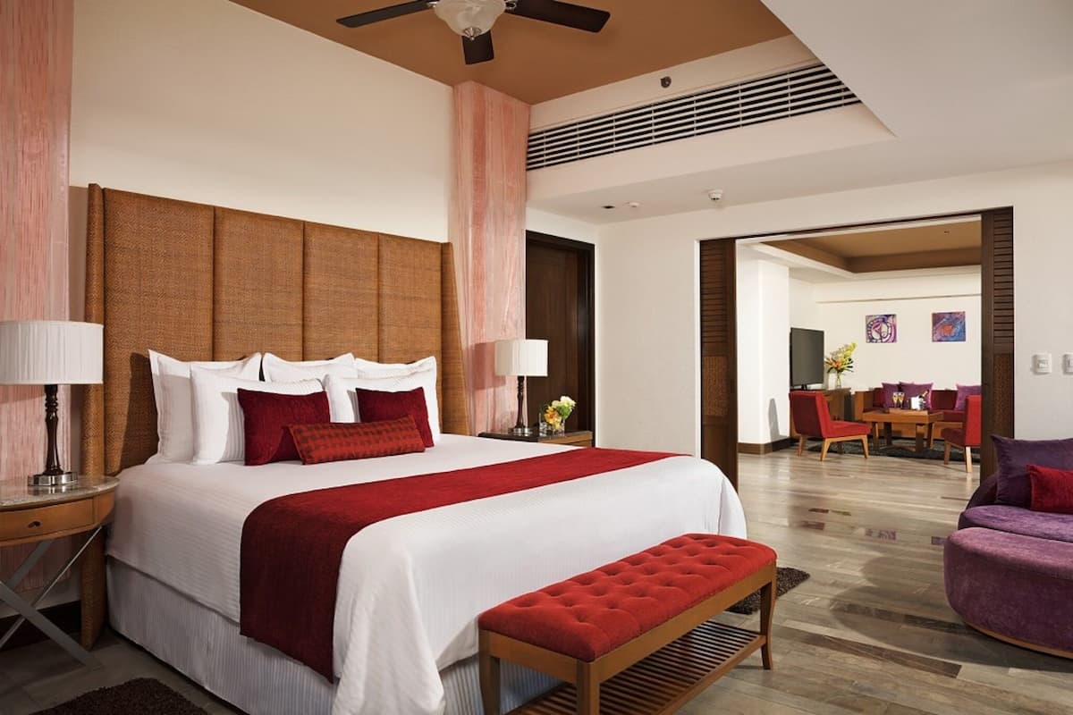 Ein Hotelzimmer mit einem großen Bett, einer Sitzbank, einem Essbereich und einem Deckenventilator.