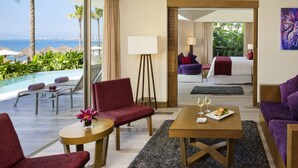 Ein Hotelzimmer mit Meerblick, ein Bett, ein Esstisch mit einer Speiseplatte und eine Sitzecke mit einem Sessel und einem kleinen Tisch.