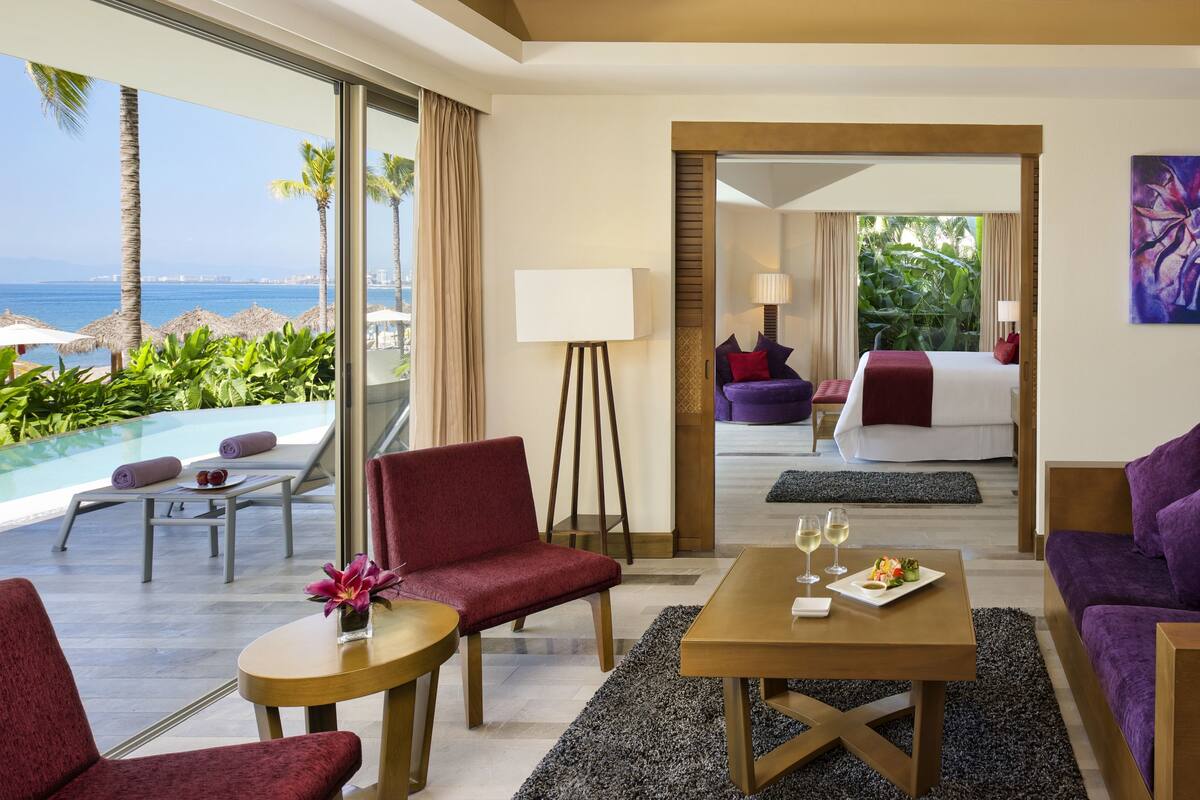 Ein Hotelzimmer mit Meerblick, ein Bett, ein Esstisch mit einer Speiseplatte und eine Sitzecke mit einem Sessel und einem kleinen Tisch.