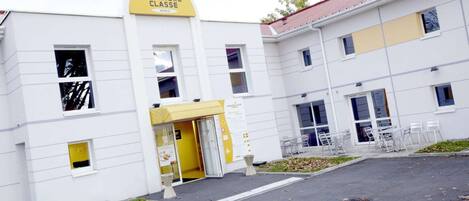 Entrada de hotel con un letrero amarillo, puerta de vidrio y una zona de estar con sillas.