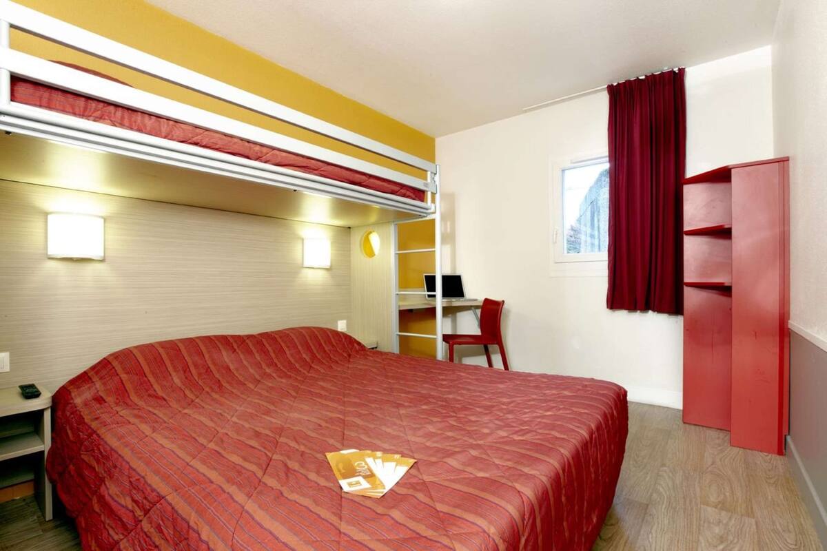 Quarto de hotel com uma cama grande, uma escrivaninha com cadeira, um guarda-roupa e uma janela com cortinas.