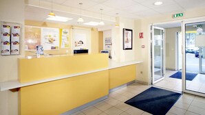 A reception area with a yellow counter, white walls, and a glass door leading outside. - Hotel Premiere Classe Pau EST Bizanos (Bizanos)