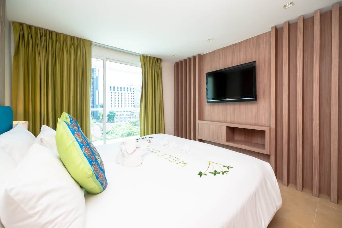 Une chambre d’hôtel avec un grand lit, un téléviseur à écran plat fixé au mur et une vue sur la ville par la fenêtre.
