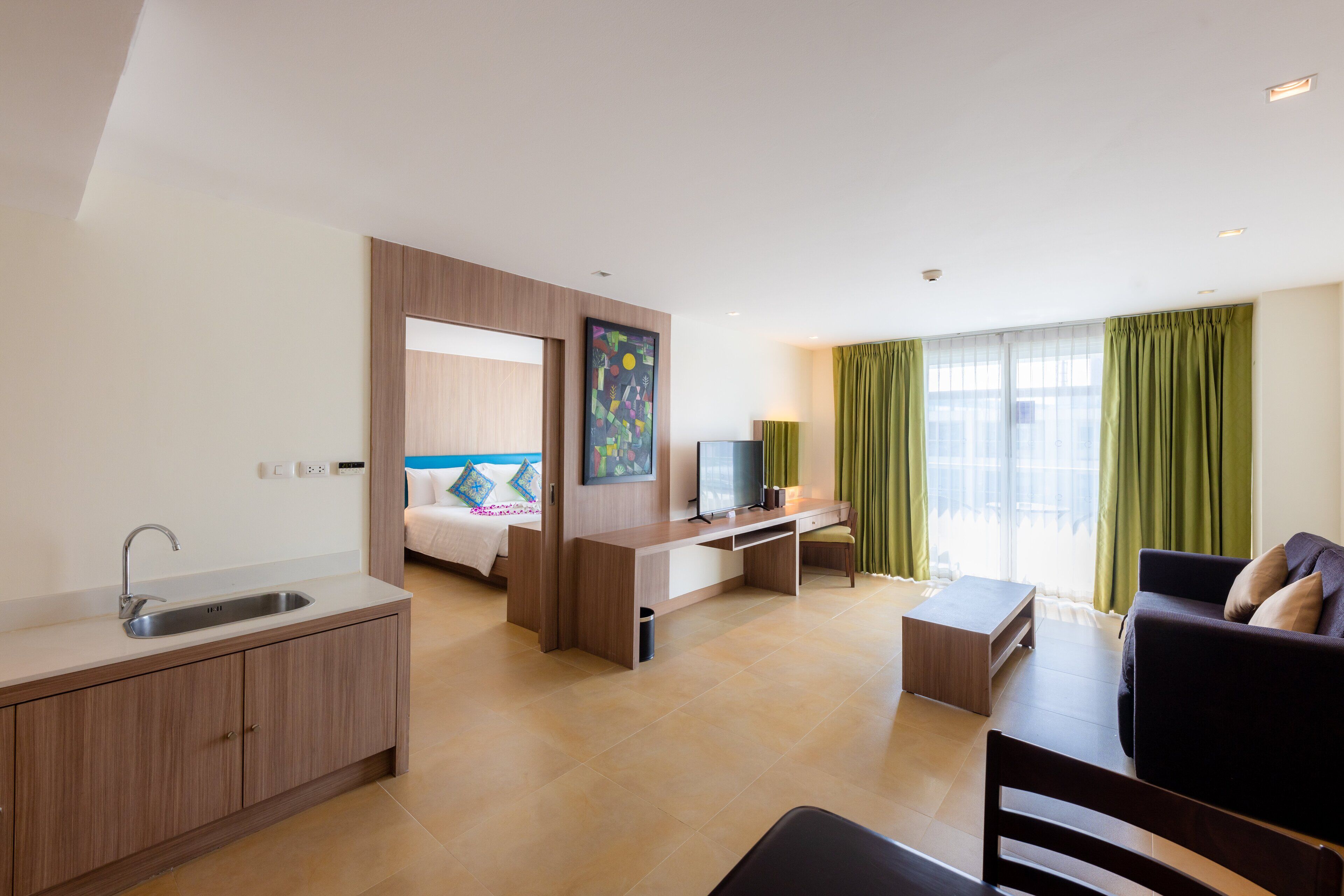 Une chambre d’hôtel moderne équipée d’une kitchenette, d’un lit, d’un bureau et d’un coin salon.