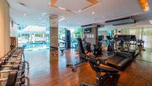 A modern gym with exercise equipment, a reception area, and large windows overlooking a pool.