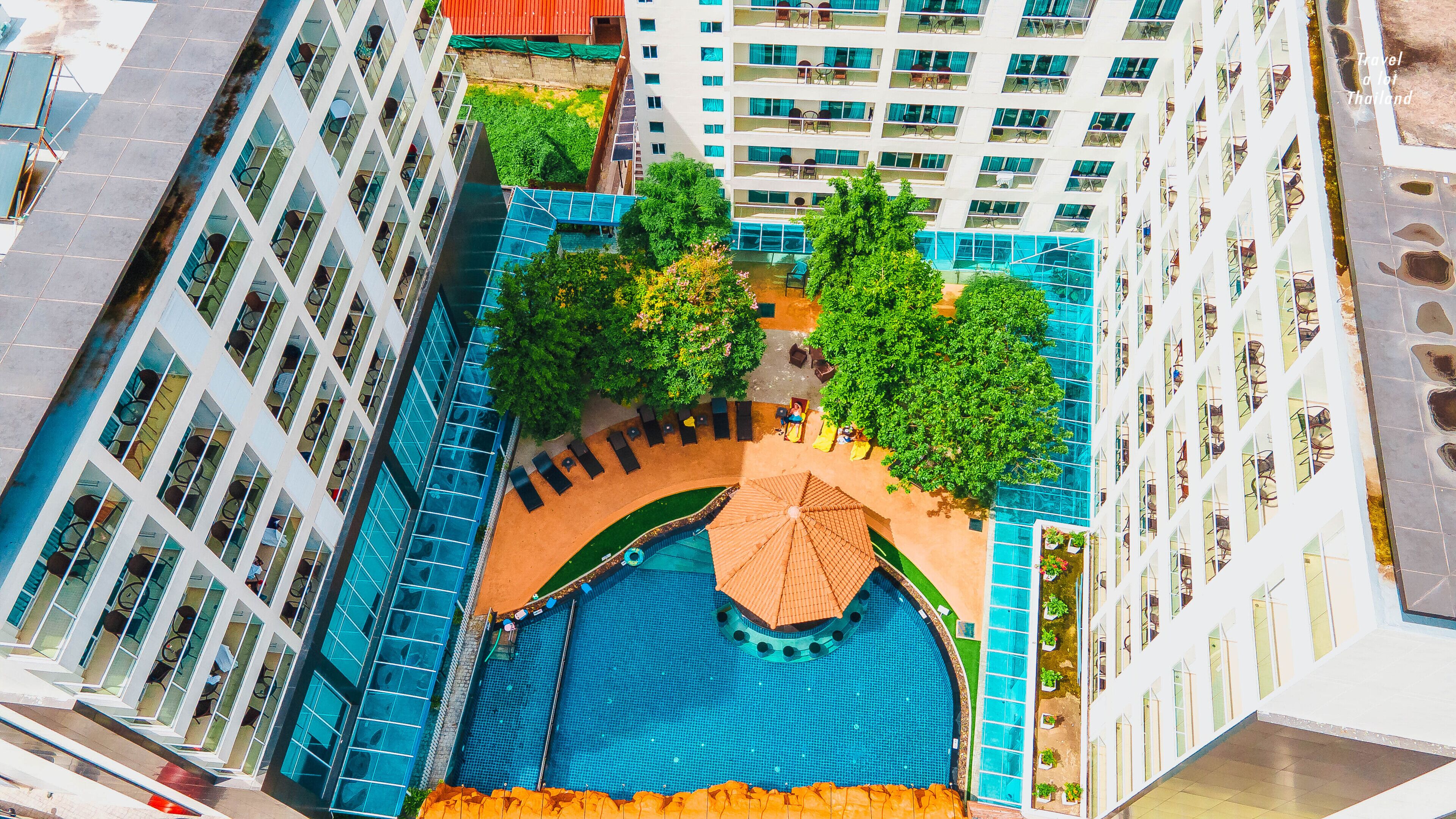 A rooftop pool area with a blue pool, surrounded by lounge chairs and umbrellas, set against a backdrop of high-rise buildings.