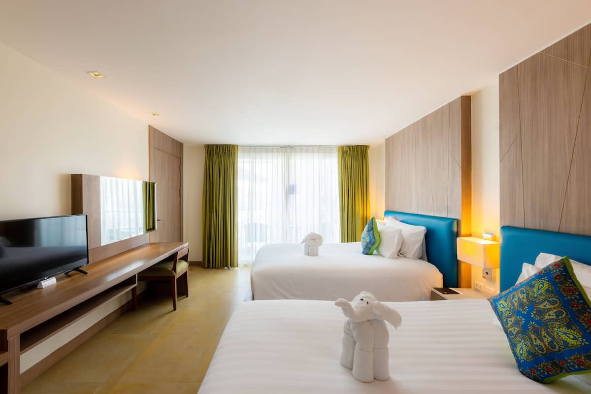 Une chambre d’hôtel équipée d’un téléviseur à écran plat, de deux lits, d’un meuble pour la télévision, d’un bureau et d’une fenêtre avec des rideaux.