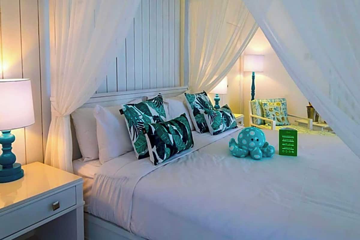 Ein Schlafzimmer mit Himmelsbett, weißer Bettwäsche und Kissen mit tropischem Dekor.
