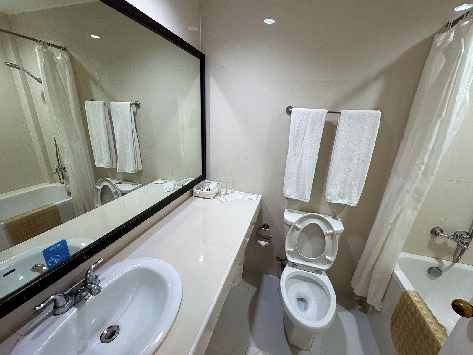 A modern bathroom with a large mirror, a white sink, a toilet, and a bathtub.