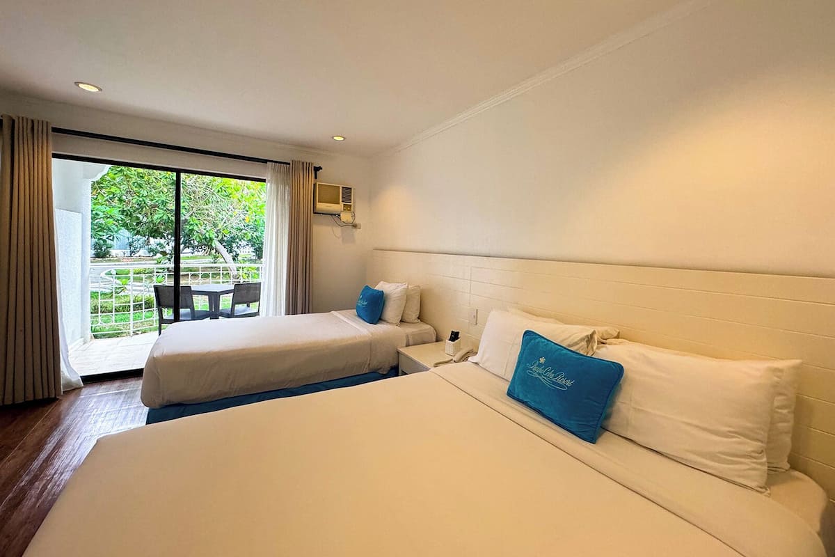 Ein Hotelzimmer mit zwei Betten, einem großen Fenster und Blick auf Grünfläche.