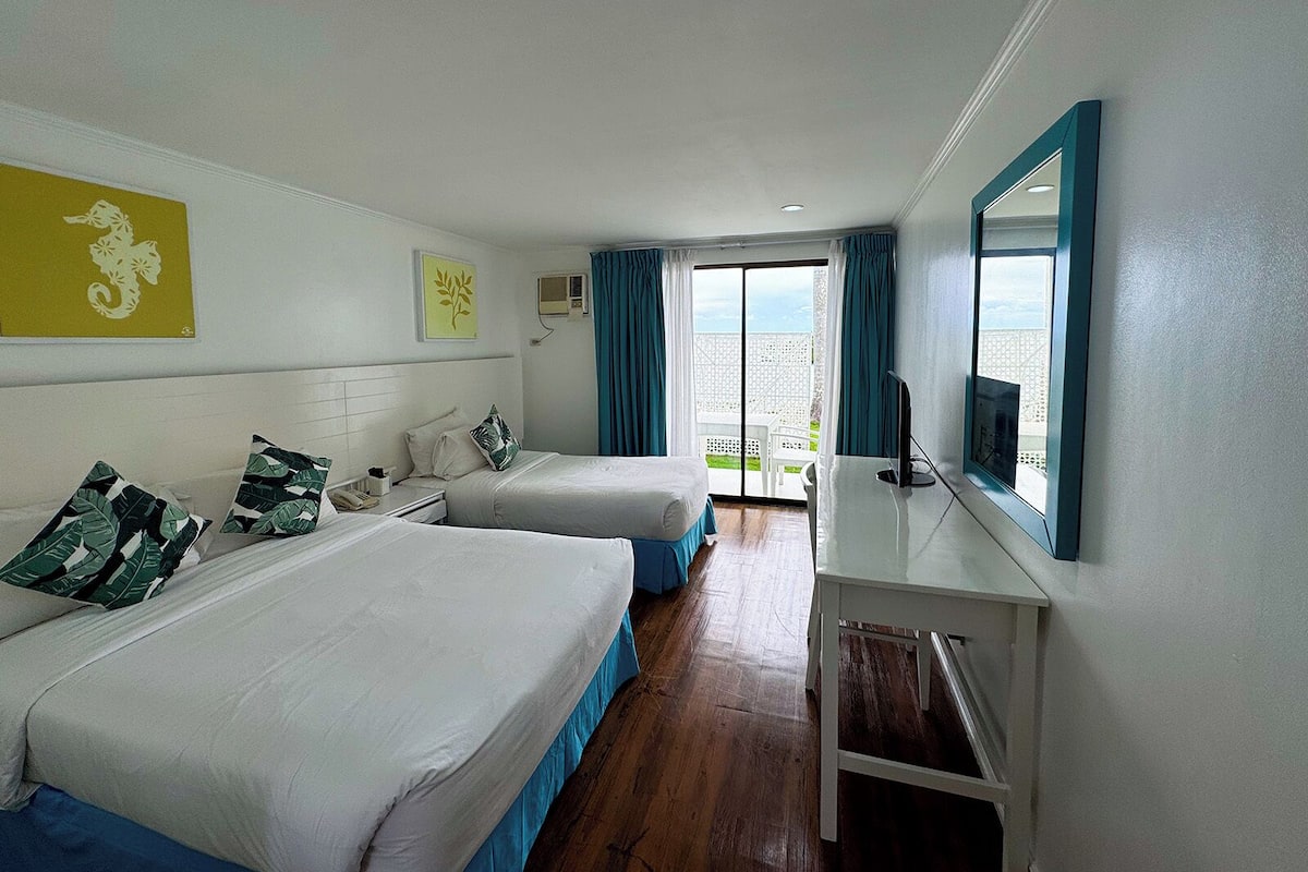Ein Hotelzimmer mit zwei Betten, einem Schreibtisch, einem Fernseher und einem Balkon mit Blick.