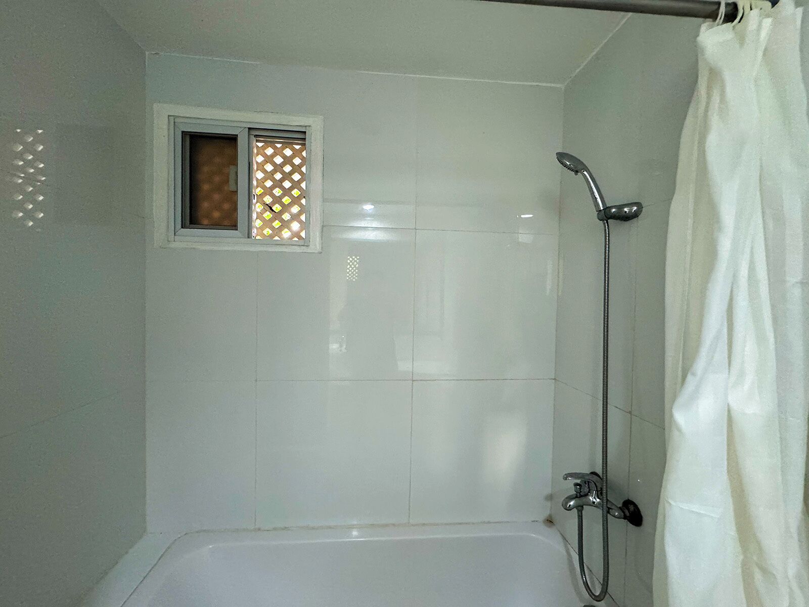 A bathroom with a bathtub, a shower, and a window with a lattice design.