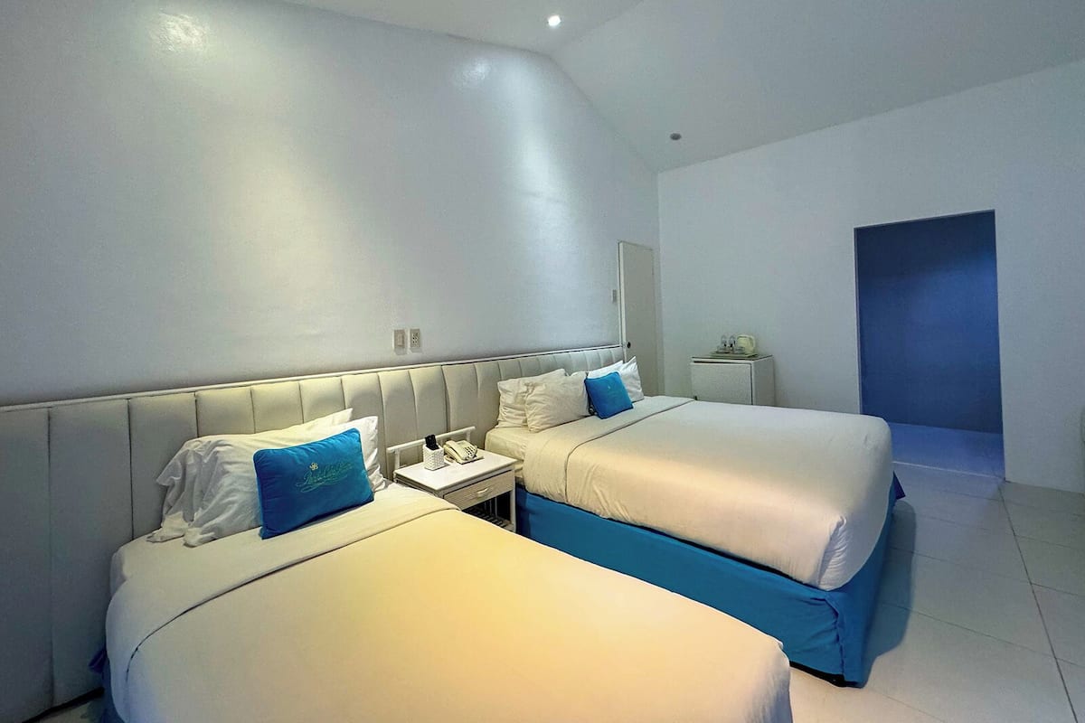 Ein Hotelzimmer mit zwei Betten, einem kleinen Nachttisch mit Telefon und einem Deckenventilator.