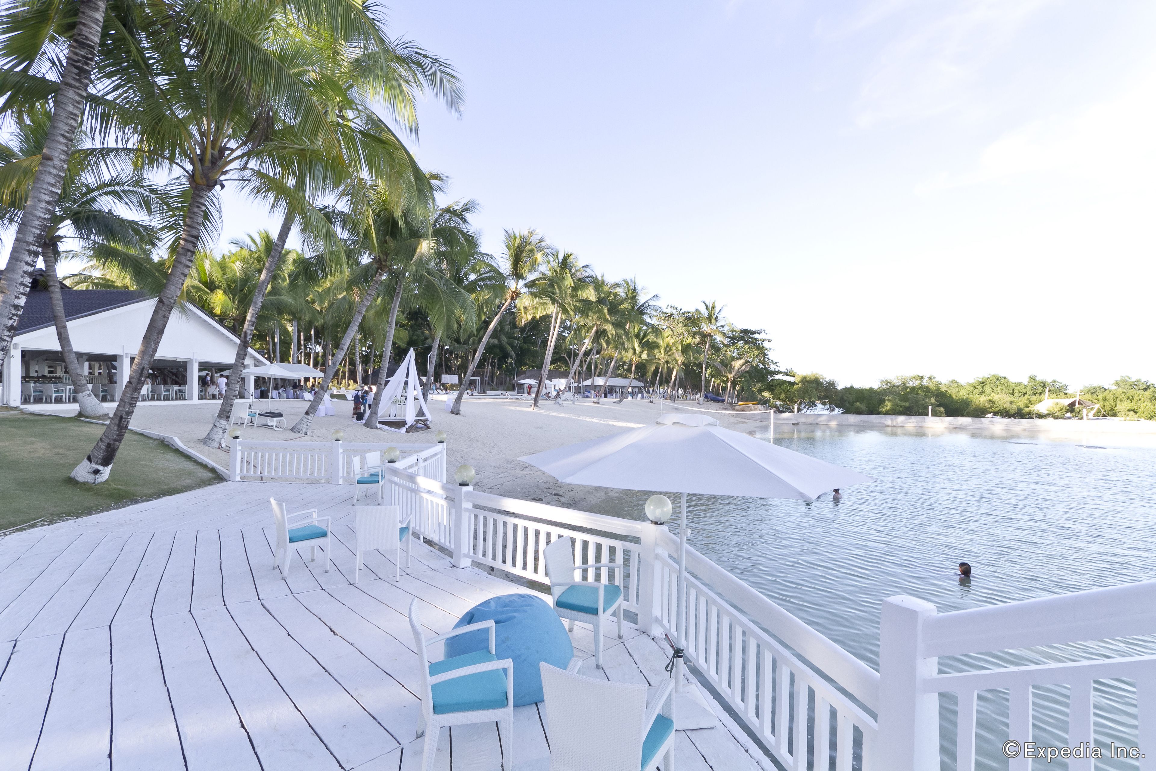 A deck with white railings and blue chairs overlooking a pool and beach area.
