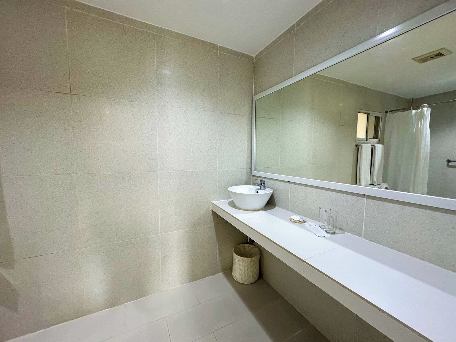 Un baño moderno con un lavamanos blanco, un espejo grande y suelo de baldosas.