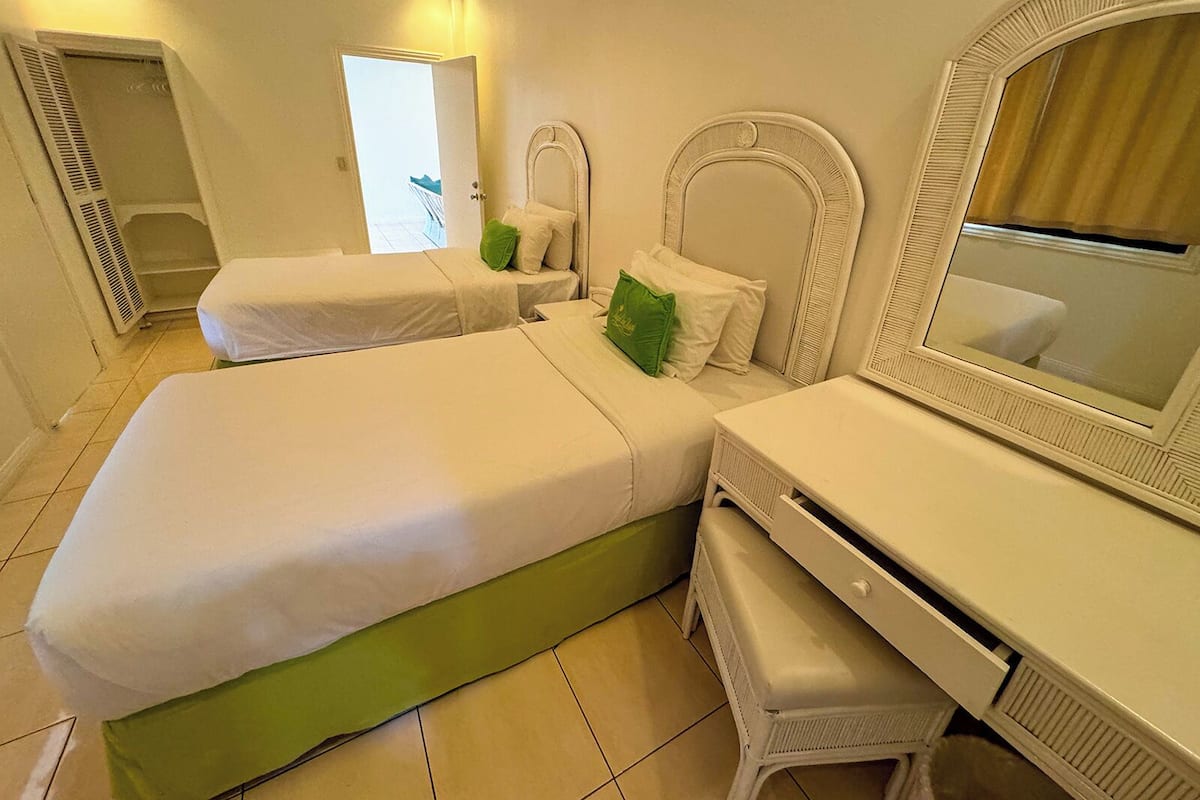 Ein Hotelzimmer mit zwei Betten, einem Schminktisch mit Spiegel und einem Fenster mit Vorhängen.