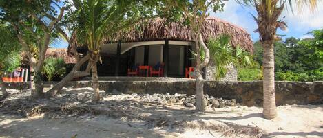 A beachside building with a thatched roof, surrounded by palm trees and a sandy area.