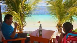 Un área de estar junto a la playa con una mesa, una botella y una copa.