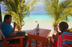 A beachside seating area with a table, a bottle, and a glass.