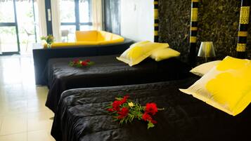 A hotel room with two beds, a yellow chair, a small table, and a window with curtains.