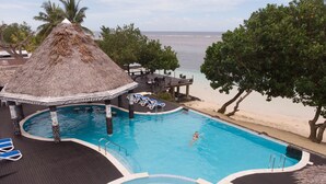 Zona de piscina con una estructura de techo de paja, sillas de descanso y vista a la playa.