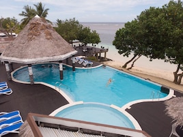 A pool area with a thatched-roof structure, lounge chairs, and a view of the beach.