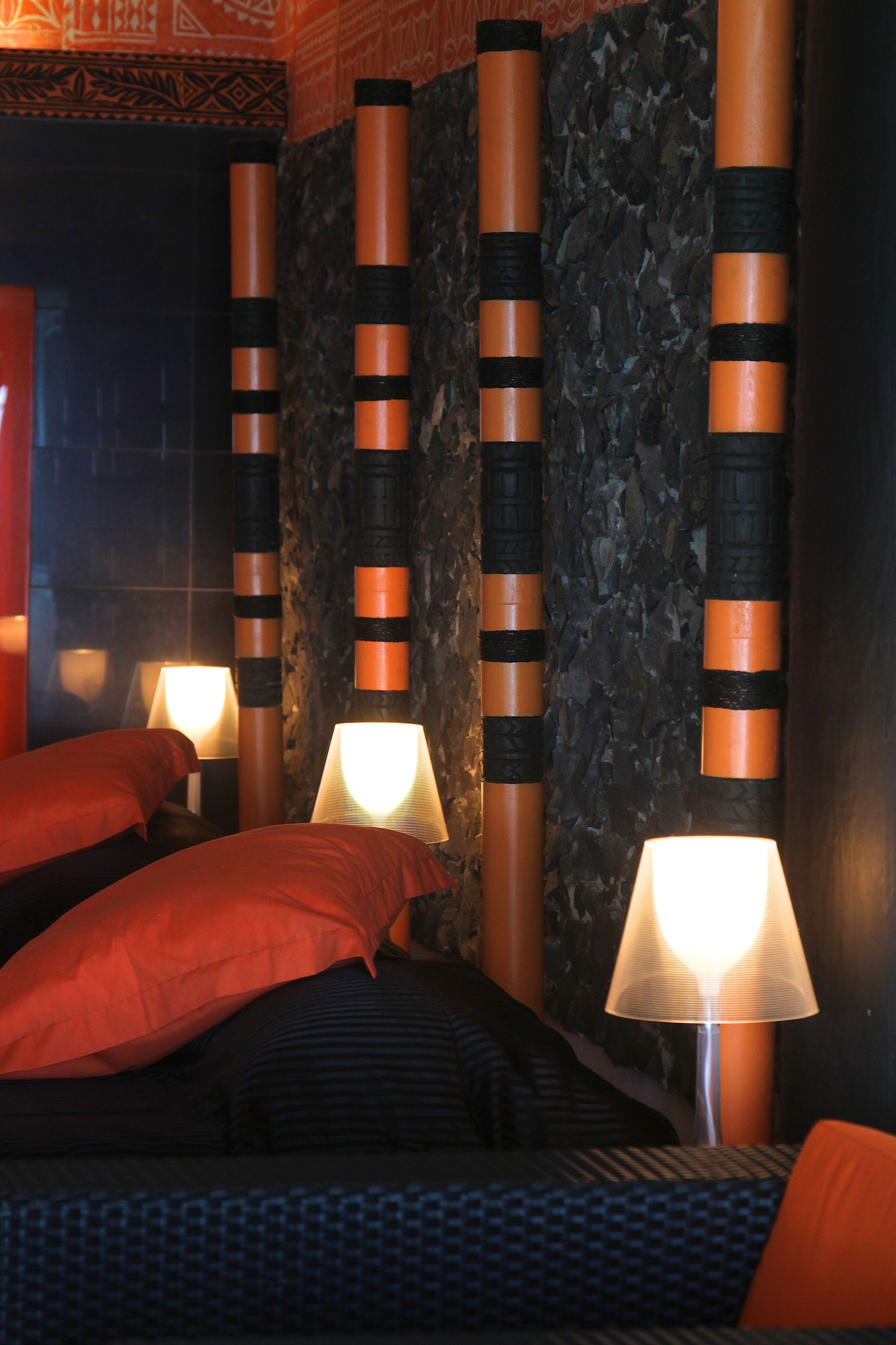 A hotel room with a bed, pillows, a lamp, and decorative pillars.