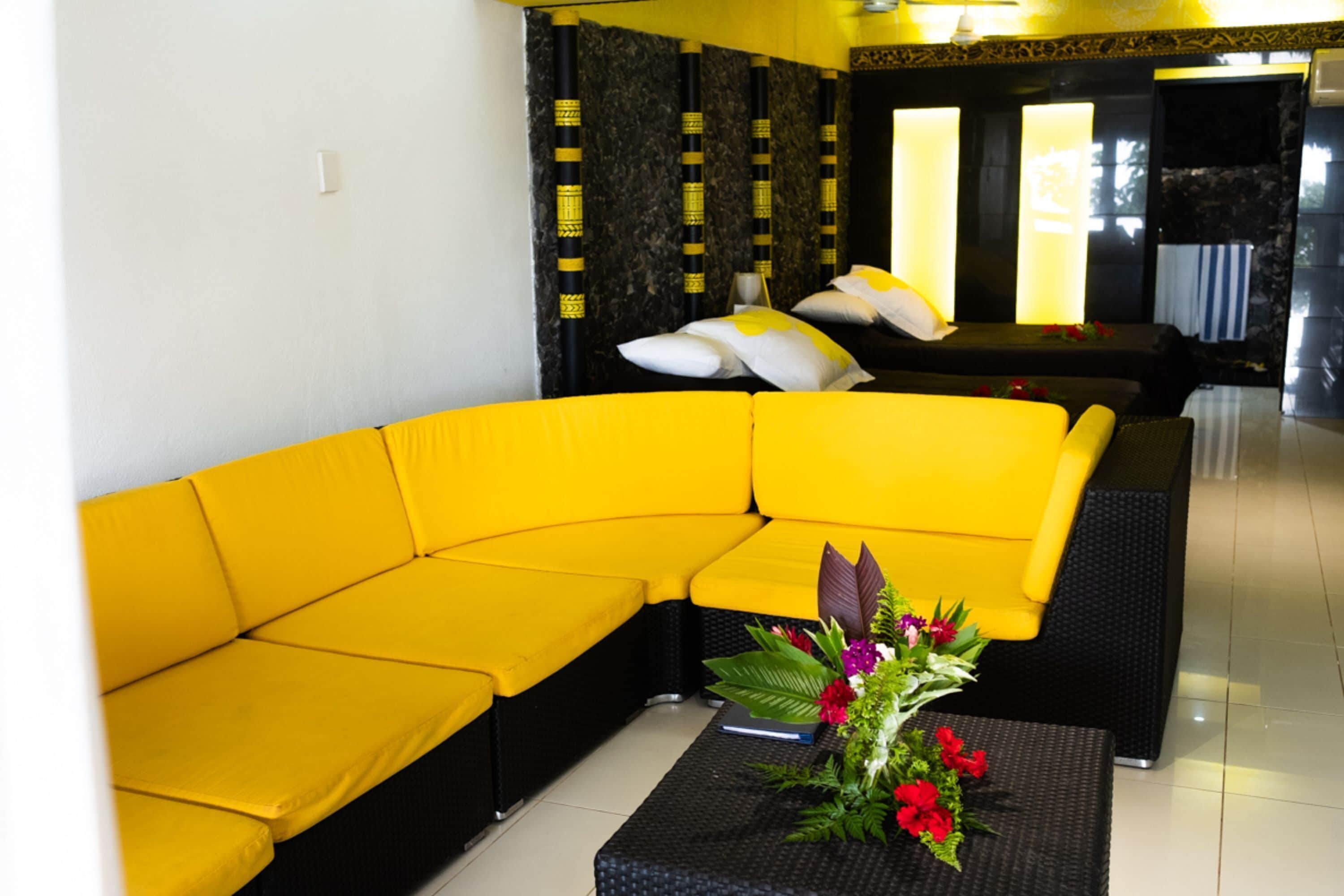 A yellow sectional sofa in a modern living room with a black coffee table and a floral centerpiece.