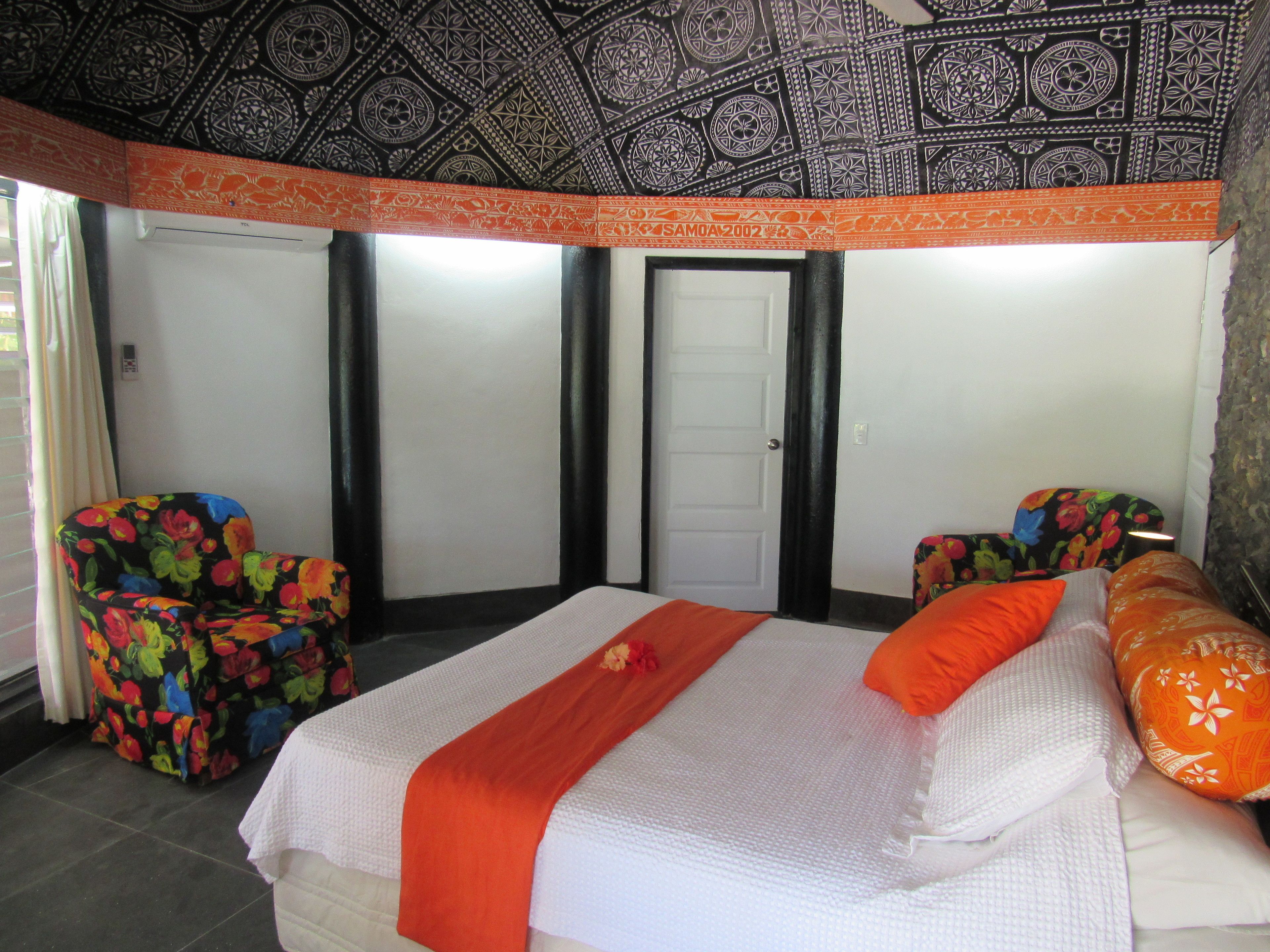 A hotel room with a bed, two chairs, a wardrobe, and a patterned ceiling.