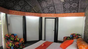 A hotel room with a bed, two chairs, a wardrobe, and a patterned ceiling.