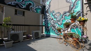 A courtyard with a mural, potted plants, and a vintage bicycle. - Hostel Zen (Yokohama)