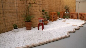 Un jardín con senderos de grava blanca, paredes de bambú y diversas plantas en macetas.