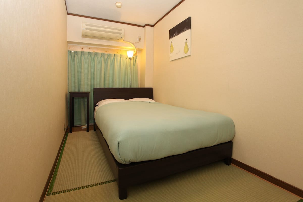 A single bed in a room with a headboard, a bedside table, and a wall-mounted air conditioner.