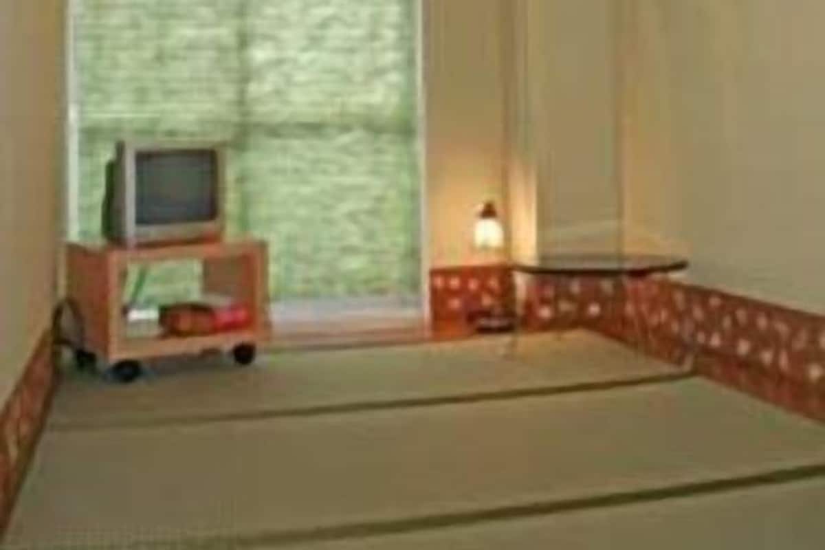 A room with a sloped ceiling, a television on a stand, a window with blinds, and a patterned wall.
