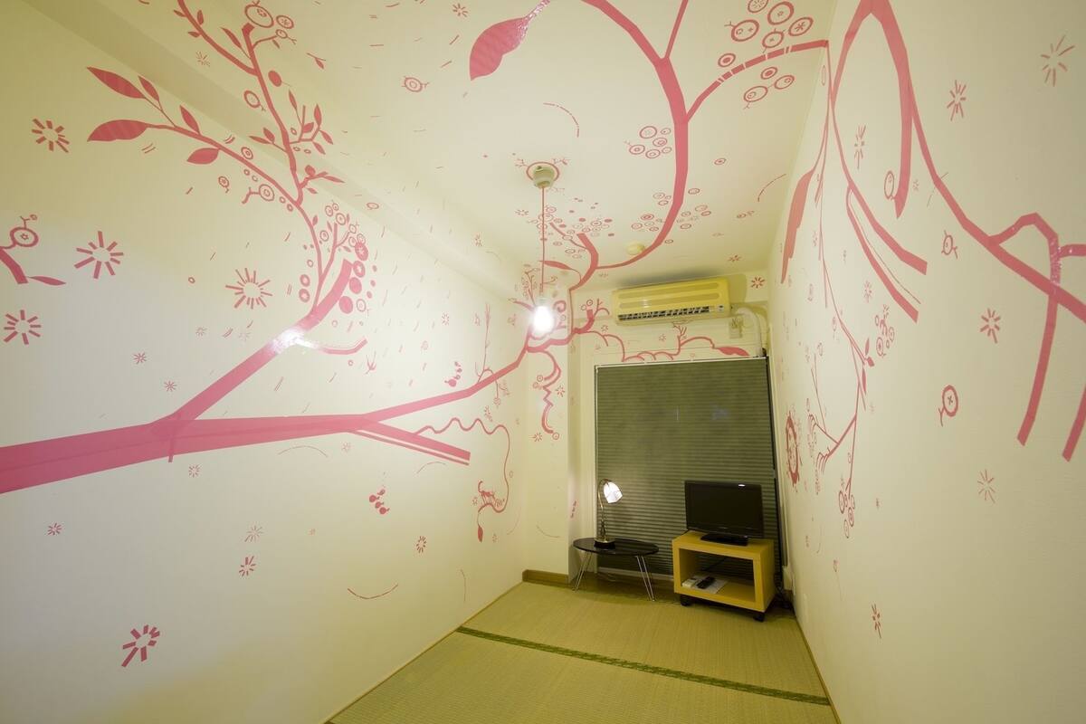 A room with a tree mural on the walls, a television, and a small table with a lamp.