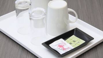 A tray with a white mug, a glass, a small bottle, and a black dish containing two packets.