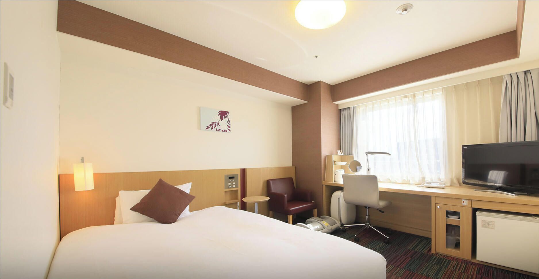 Une chambre d’hôtel équipée d’un lit, d’un bureau, d’une chaise, d’une télévision et d’un petit réfrigérateur.