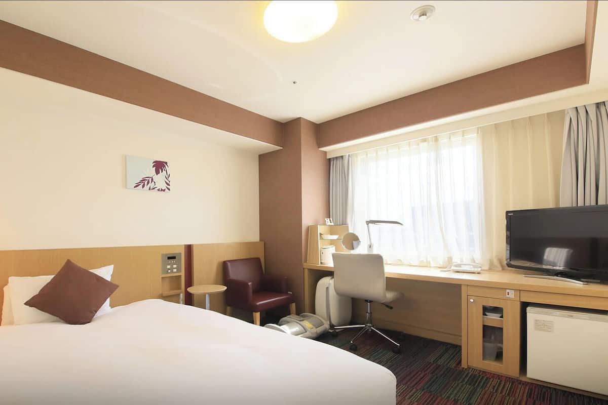 Een hotelkamer met een bed, bureau, stoel, televisie en een kleine koelkast.