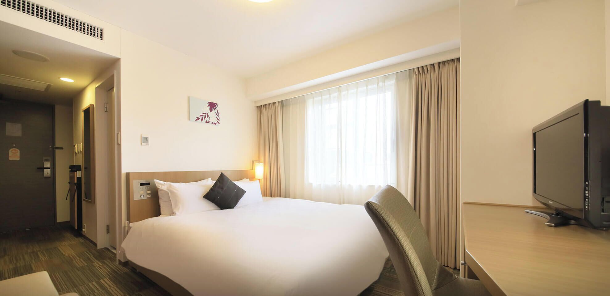 Une chambre d’hôtel avec un grand lit, une télévision et une fenêtre avec des rideaux.