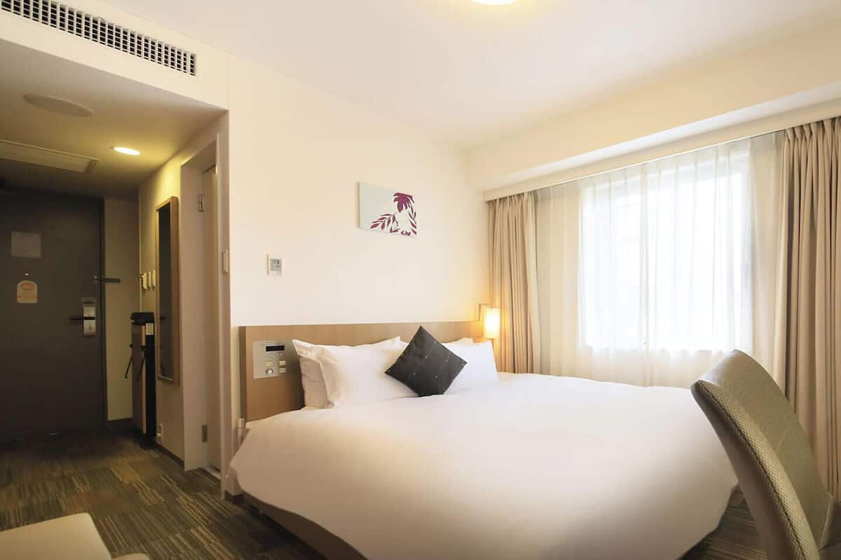 Een hotelkamer met een groot bed, een televisie en een raam met gordijnen.