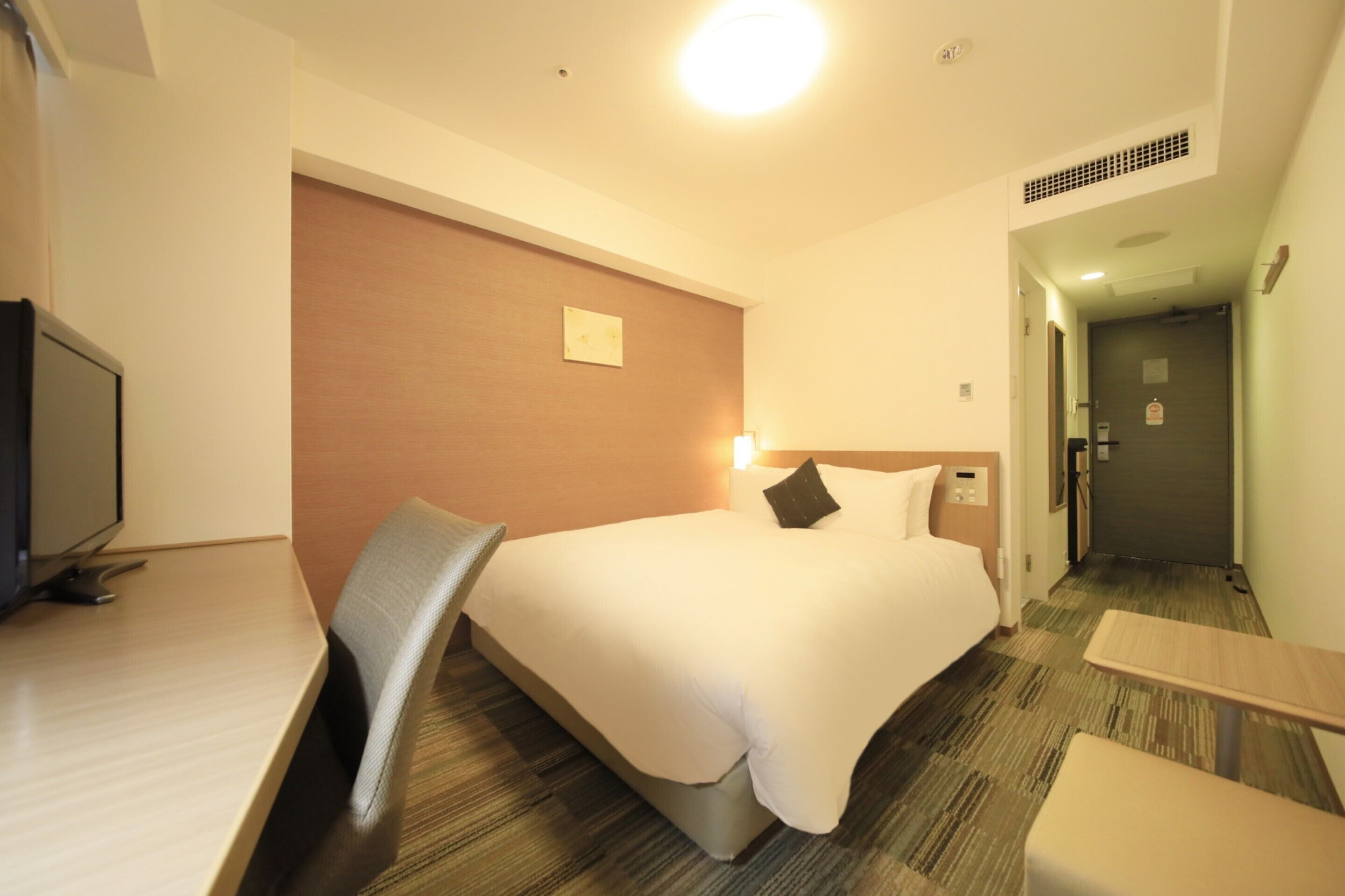 A hotel room with a bed, a desk, a chair, a television, and a door leading to another room.