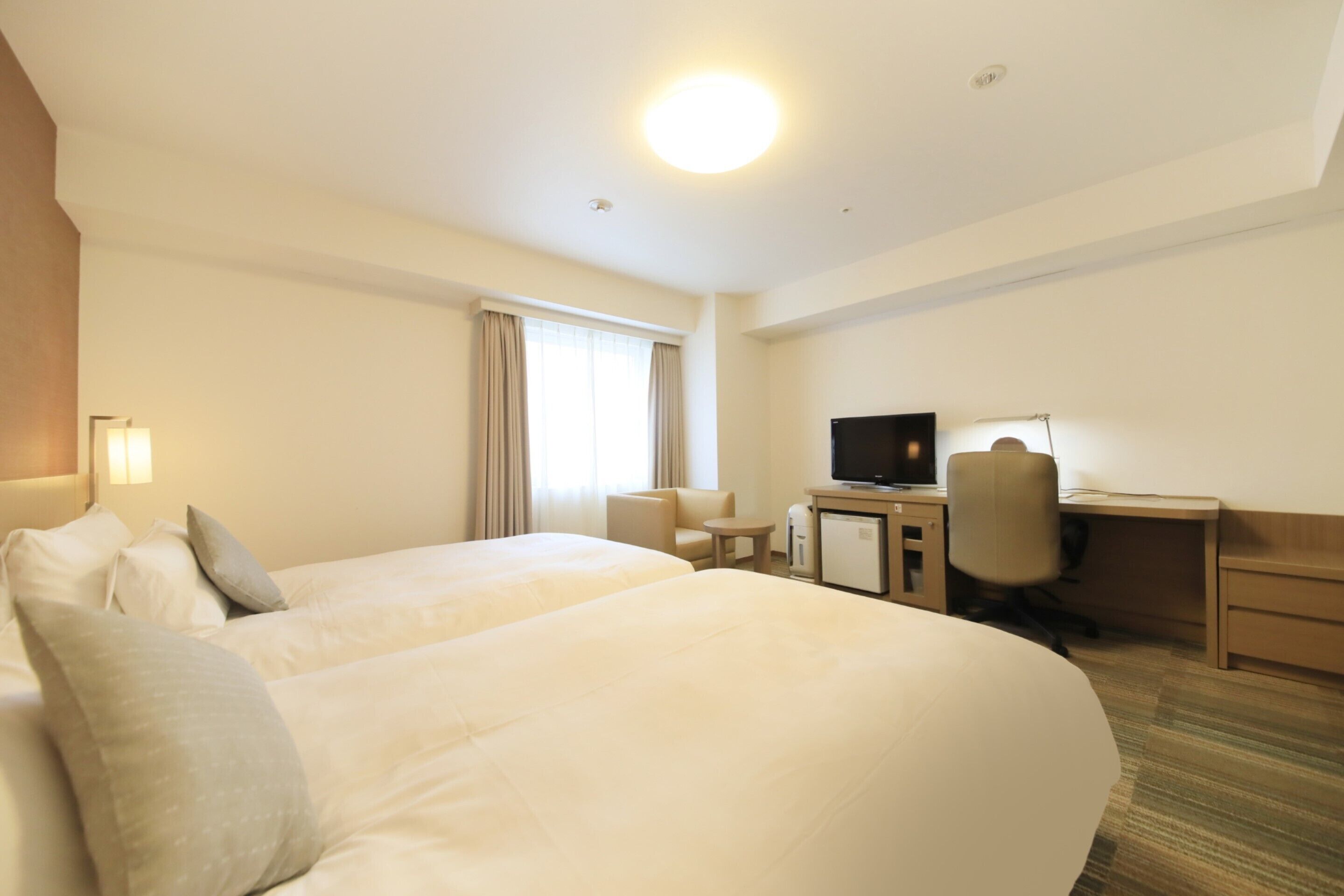 A hotel room with two beds, a desk, a chair, a television, and a small table.