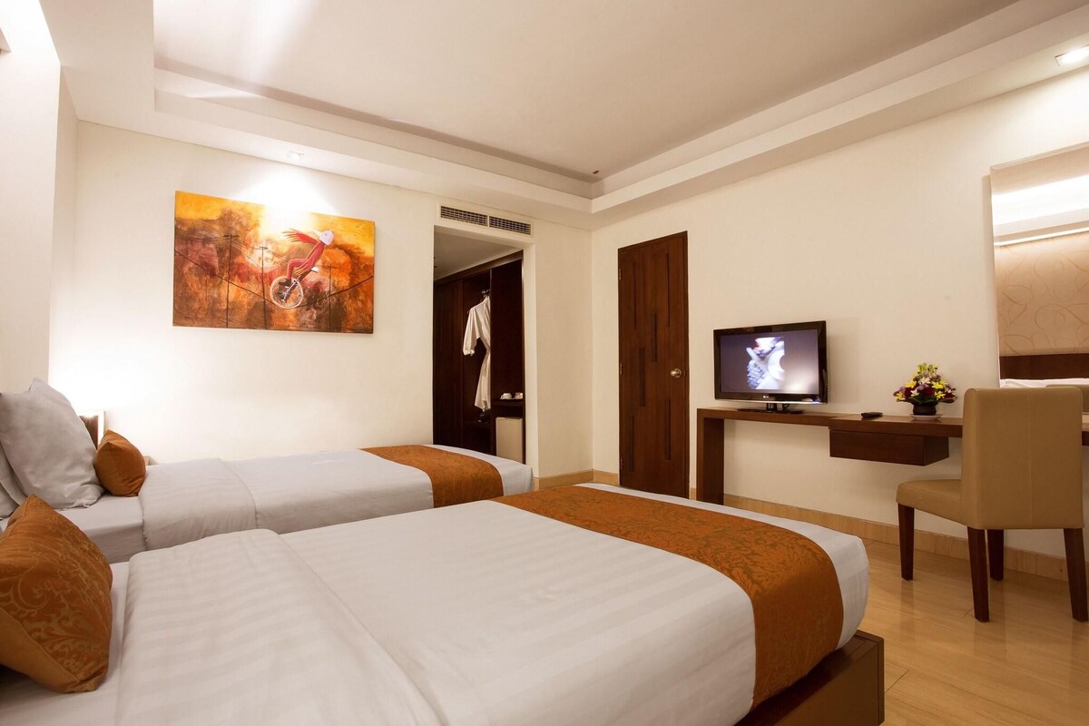 A hotel room with two beds, a TV, a desk, and a chair.