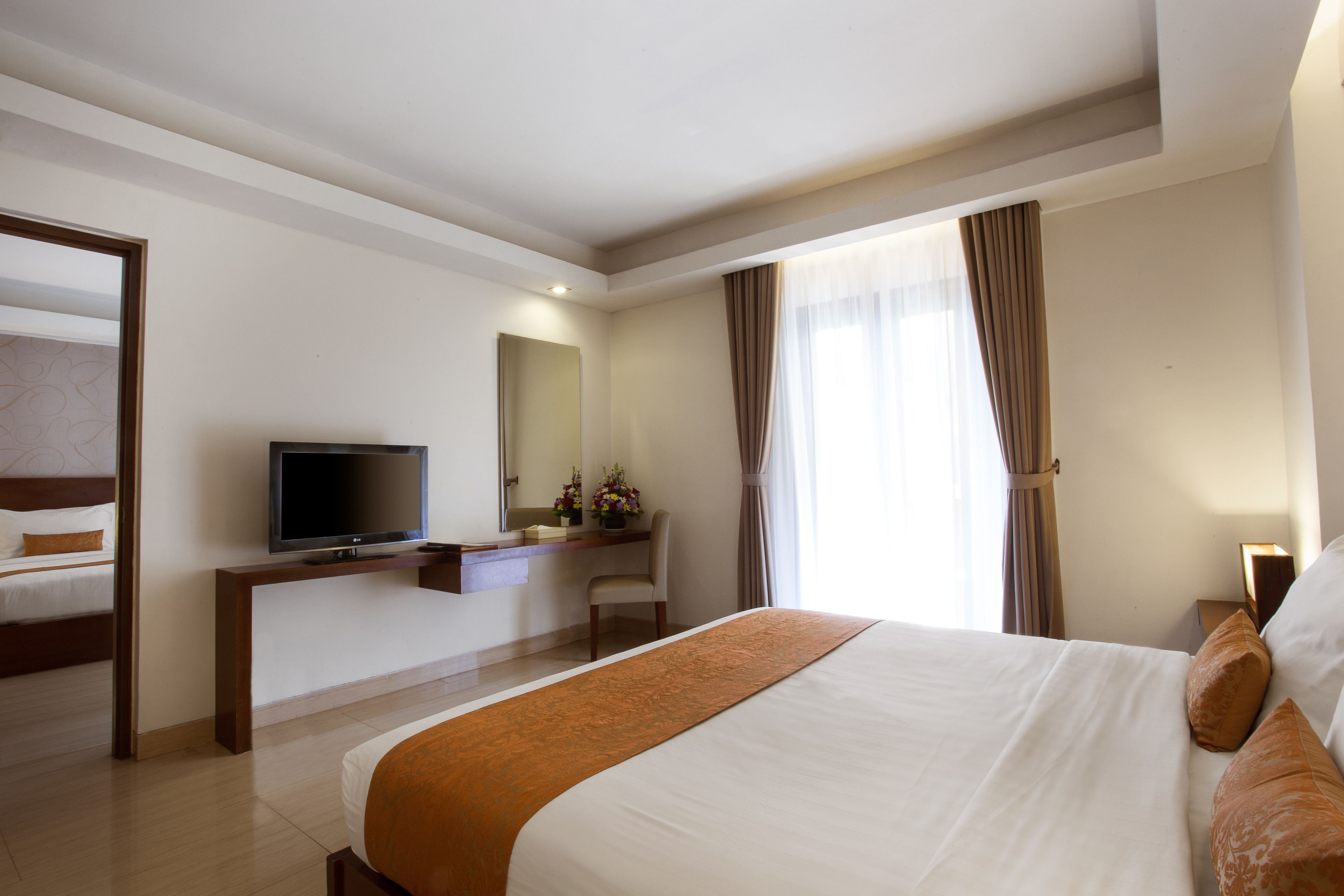 Una habitación de hotel con una cama grande, televisión, escritorio con silla y ventana con cortinas.
