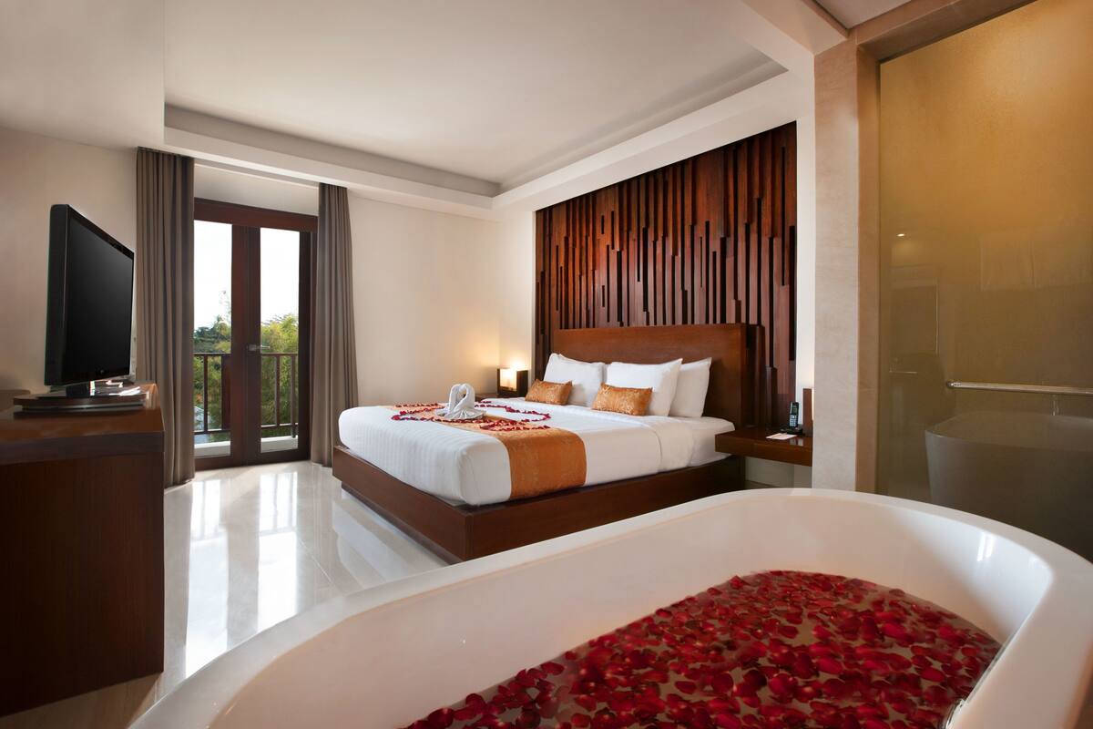 A modern hotel room with a large bed, a TV, a bathroom with a bathtub, and a balcony with curtains.