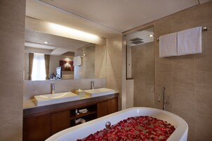 Un baño moderno con una bañera grande llena de pétalos de rosa, un tocador doble y una ducha a ras de suelo.