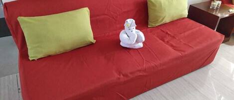 Un divano rosso con cuscini verdi e un oggetto decorativo bianco.